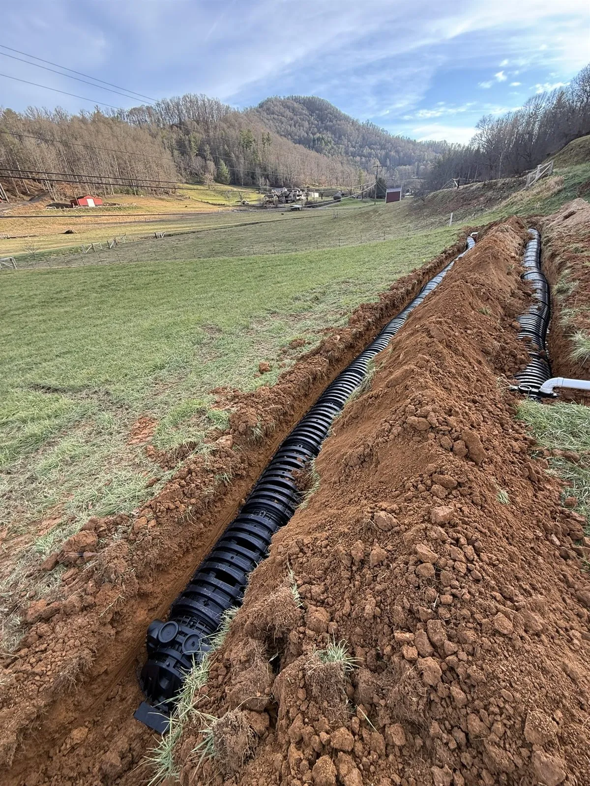 Drainage trench and pipe run cut across a sloped site near Bakersville, NC