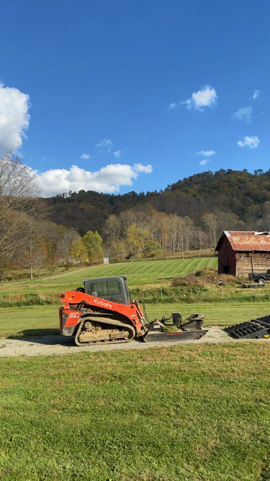 Compact track loader on a mountain pasture with a barn in Western NC