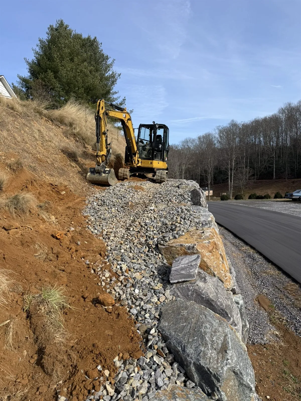 Excavator setting large boulders to build a retaining wall along a road in Western NC