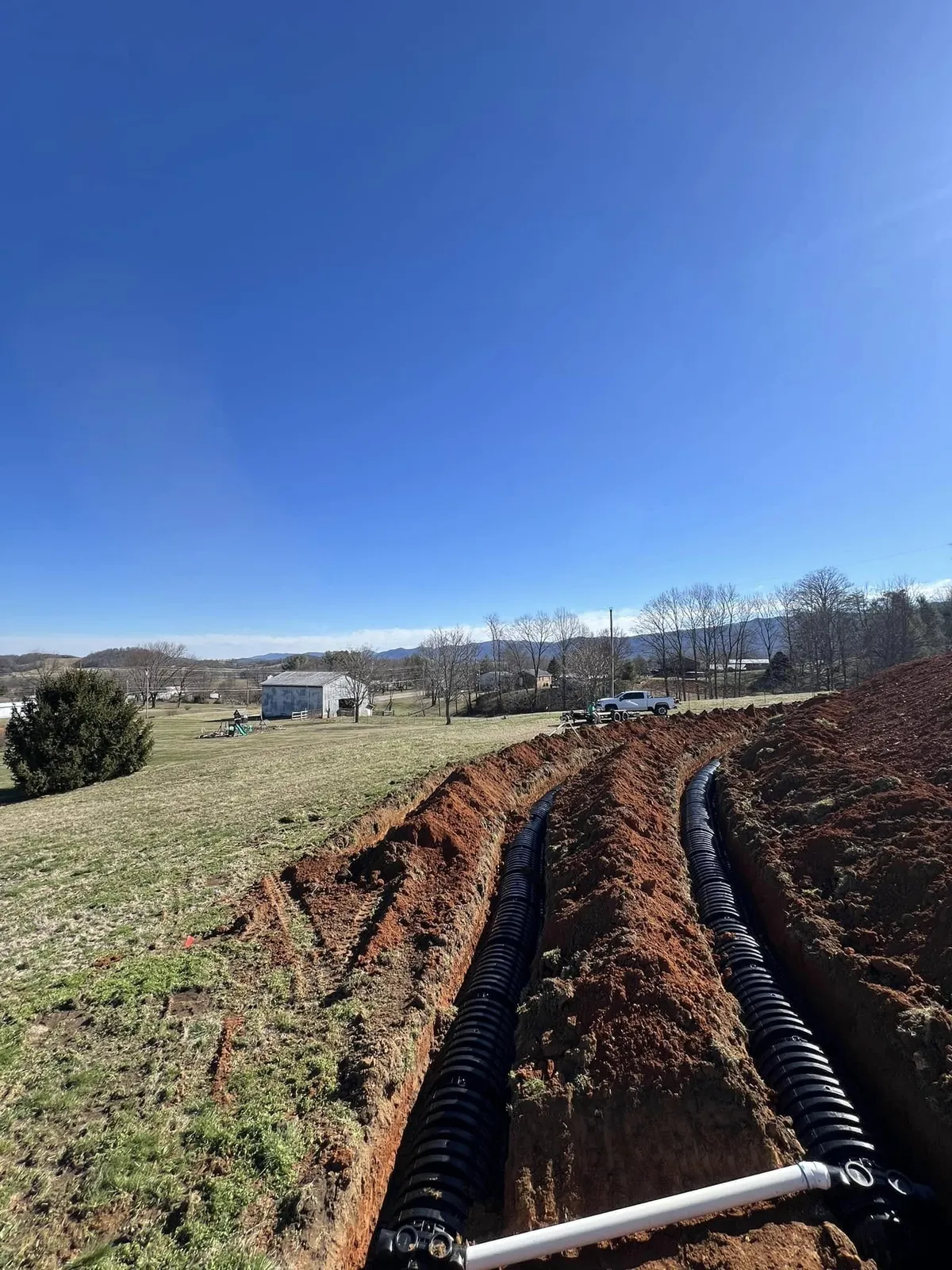 Twin corrugated drainage lines run in an open trench, mountain backdrop