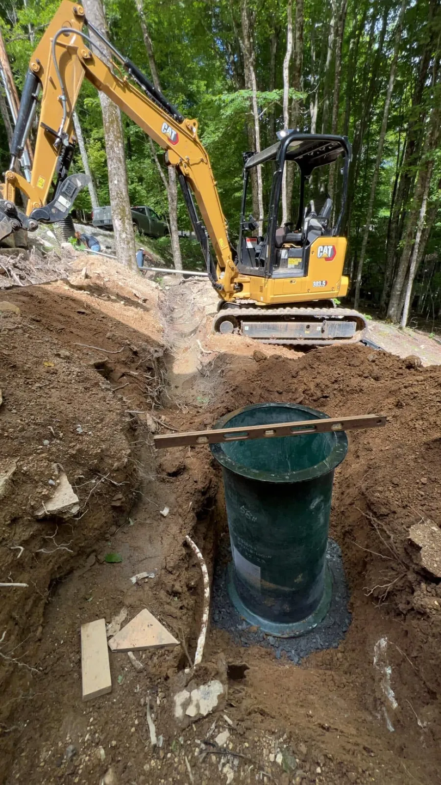 Compact excavator setting the septic pump basin in an excavation on a residential site near Burnsville, NC